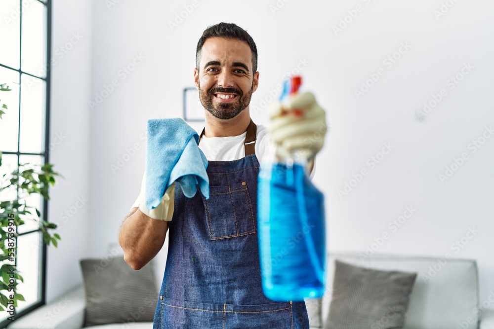 Wall mural young hispanic man smiling confident holding sprayer at home - Wall murals