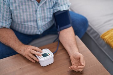 Middle age grey-haired man measuring pulse using tensiometer at home