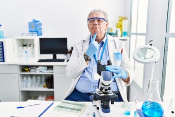 Senior caucasian man working at scientist laboratory thinking concentrated about doubt with finger...