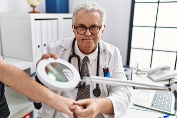 Middle age grey-haired man wearing dermatologist uniform using loupe at dermatology clinic