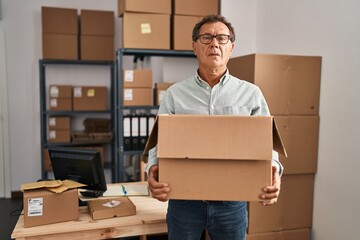 Senior man working at small business ecommerce holding carboard bx relaxed with serious expression on face. simple and natural looking at the camera.