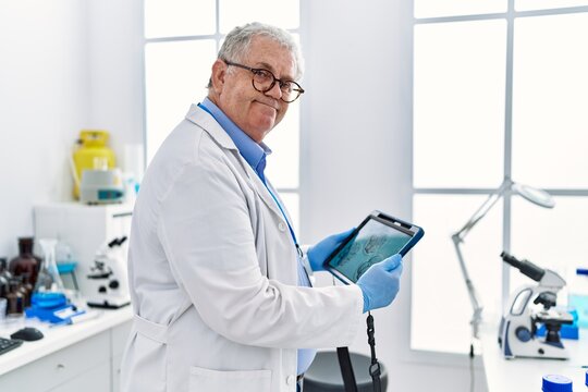 Middle age grey-haired man wearing scientist uniform looking embryology image touchpad at laboratory