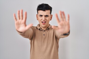 Non binary person standing over isolated background doing stop gesture with hands palms, angry and...