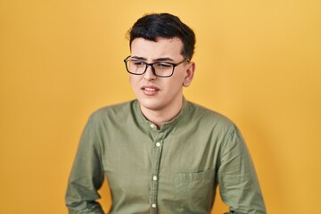 Non binary person standing over yellow background with hand on stomach because indigestion, painful illness feeling unwell. ache concept.