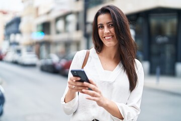 Young beautiful hispanic woman smiling confident using smartphone at street