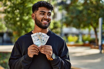 Young arab man smiling confident holding sol peruvian banknotes at park - obrazy, fototapety, plakaty