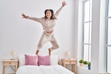 Young hispanic woman smiling confident jumping on bed at bedroom