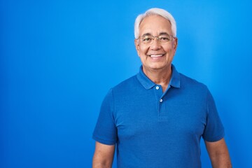 Middle age man with grey hair standing over blue background with a happy and cool smile on face....