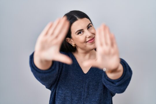 Young brunette woman standing over isolated background doing frame using hands palms and fingers, camera perspective