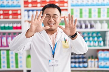 Chinese young man working at pharmacy drugstore showing and pointing up with fingers number ten while smiling confident and happy.