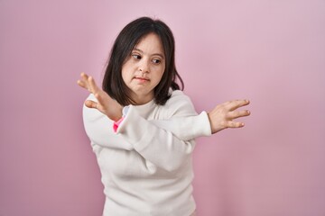 Woman with down syndrome standing over pink background rejection expression crossing arms doing negative sign, angry face