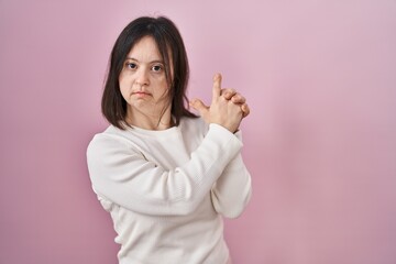 Woman with down syndrome standing over pink background holding symbolic gun with hand gesture, playing killing shooting weapons, angry face