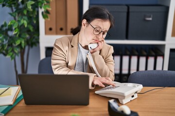 Fototapeta premium Young woman with down syndrome business worker using laptop talking on the telephone at office