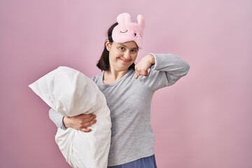 Woman with down syndrome wearing sleeping mask hugging pillow looking confident with smile on face, pointing oneself with fingers proud and happy.