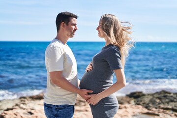 Man and woman couple standing together touching belly at seaside