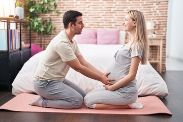Man and woman couple expecting belly doing prepartum exercise at bedroom