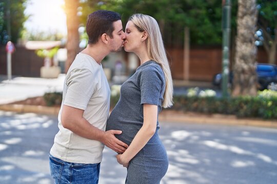 Man and woman couple standing together touching belly kissing at street