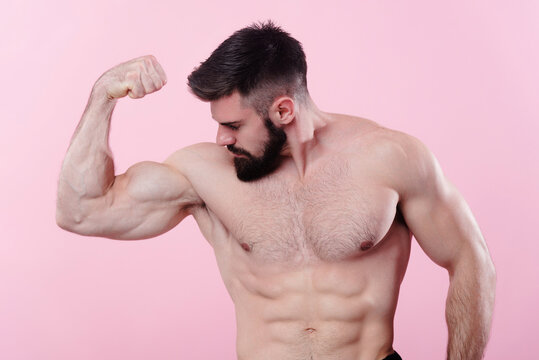 Handsome bodybuilder flexing his bicep muscle, showing off a power pose, studio image on pink background