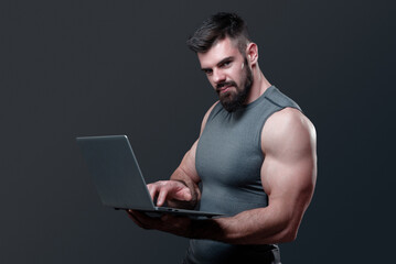 Young bodybuilder, online fitness coach, using a laptop and a headset to talk to an online client, studio image - 538745174