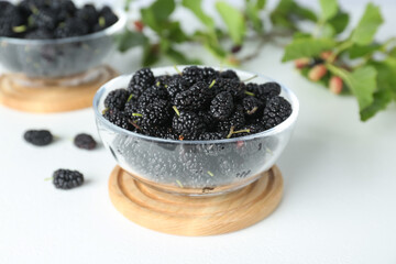 Fototapeta na wymiar Delicious ripe black mulberries in glass bowl on white table, closeup