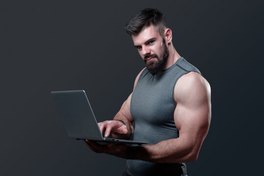 Young bodybuilder, online fitness coach, using a laptop and a headset to talk to an online client, studio image