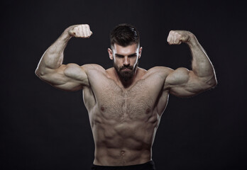 Fototapeta na wymiar Beast mode - strong shirtless man, a bodybuilder, flexing his biceps, showing off his big arms and muscular body, dark image, black background