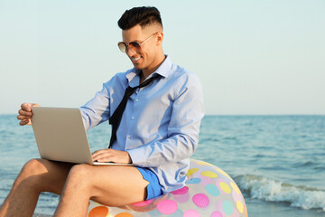 Happy businessman working with laptop on beach. Business trip