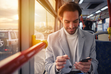 Handsome man on a bus, looking at his phone, browsing social media while commuting