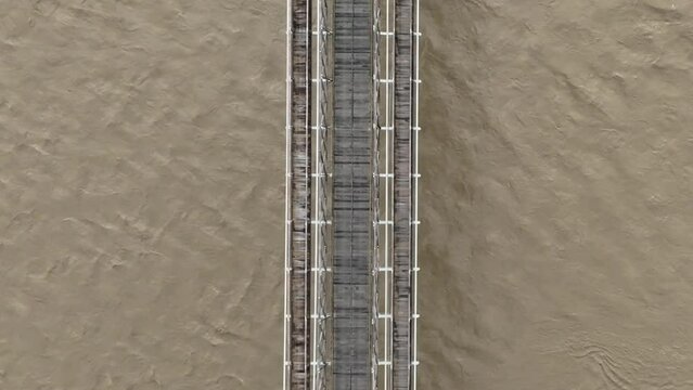 Top Down Aerial View of Old Suspension Bridge Above Flooding Muddy River