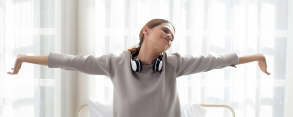 Beautiful young woman waking up in the morning and stretching sitting on bed in the bedroom at...