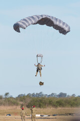 paracaidista militar proximo a tocar tierra con la mirada de sus instructores calificando sus...