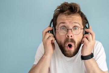 Funny man in headphones listens to music, he is surprised at what he hears, makes big eyes and...