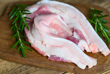 pork on wooden plate with rosemary, fresh raw streaky pork meat for cooking food, pork skin pig skin - top view