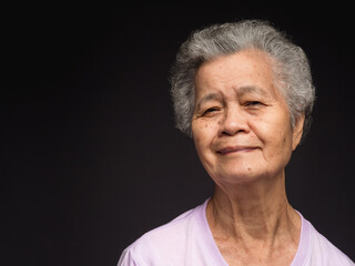 An elderly Asian woman looking at the camera with a smile while standing on a black background
