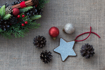Background from natural fabric. In the corner is a part of a Christmas wreath with green branches, red berries, cinnamon sticks, Christmas balls. Two fir cones and Christmas decorations. Close-up.