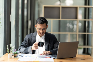 Fototapeta premium Portrait of young man sitting at his desk in the office, Businessman having coffee and doing his work in cafe.