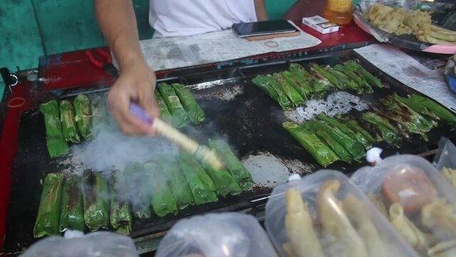 video of the process of cooking traditional Indonesian cakes "otak otak" made from fresh fish meat wrapped in banana leaves by roasting.