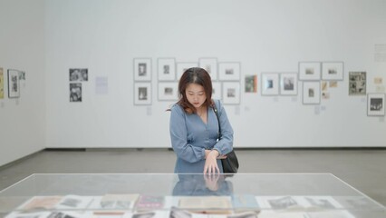 A young woman in a dress is walking and looking exhibits and artworks in a museum or art gallery