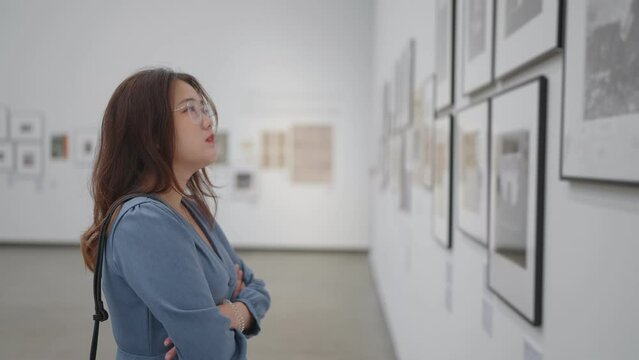 Woman wearing eyeglasses looking artworks on the wall in art gallery