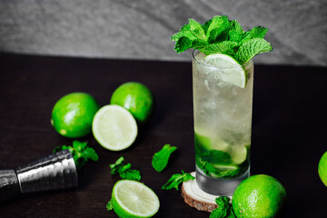 mojito cocktail with lime and mint leaves on a wooden table and grey background, refreshing cold...