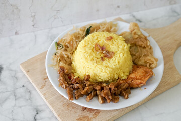 Nasi kuning, yellow rice or tumeric rice is traditional food from asia, made rice cooked with turmeric, coconut milk and spices served with egg, chicken, peanuts, chili sauce, sliced ​​cucumber, tempe