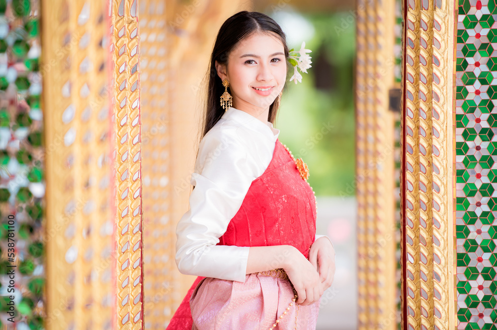 Wall mural Portrait of a beautiful woman wearing a traditional Thai dress smiling gracefully standing in a temple of Thailand