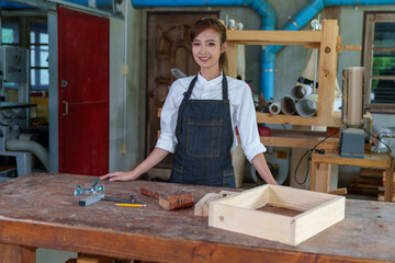 portrait of beautiful asian woman carpenter dealing with handicraft, woman has own business connected with making wooden furniture in workshop