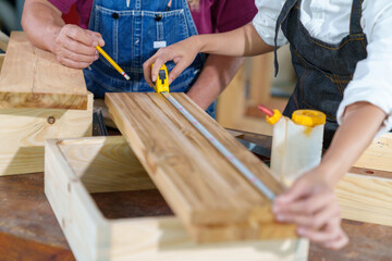 A tutor with a Female carpenter student in a workshop studying for an apprenticeship at a college using a tape measure.