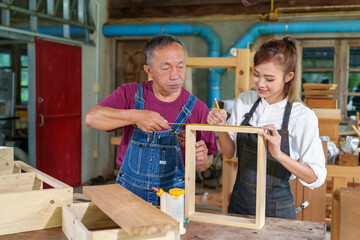 A tutor with a Female carpenter student in a workshop studying for an apprenticeship at a college using a tape measure.