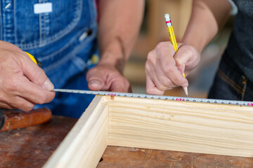 Obraz premium A tutor with a Female carpenter student in a workshop studying for an apprenticeship at a college using a tape measure.