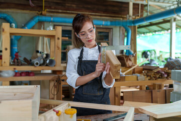 portrait of beautiful asian woman carpenter dealing with handicraft, woman has own business connected with making wooden furniture in workshop