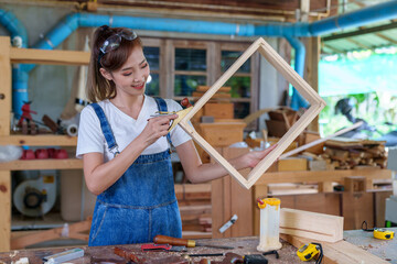 portrait of beautiful asian woman carpenter dealing with handicraft, woman has own business connected with making wooden furniture in workshop