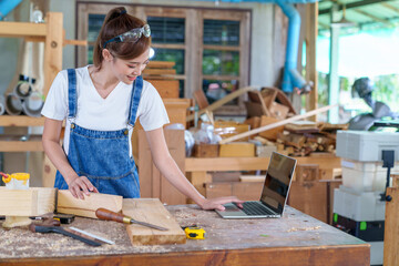 portrait of beautiful asian woman carpenter dealing with handicraft, woman has own business connected with making wooden furniture in workshop.