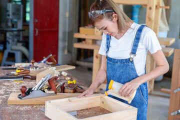 portrait of beautiful asian woman carpenter dealing with handicraft, woman has own business connected with making wooden furniture in workshop.